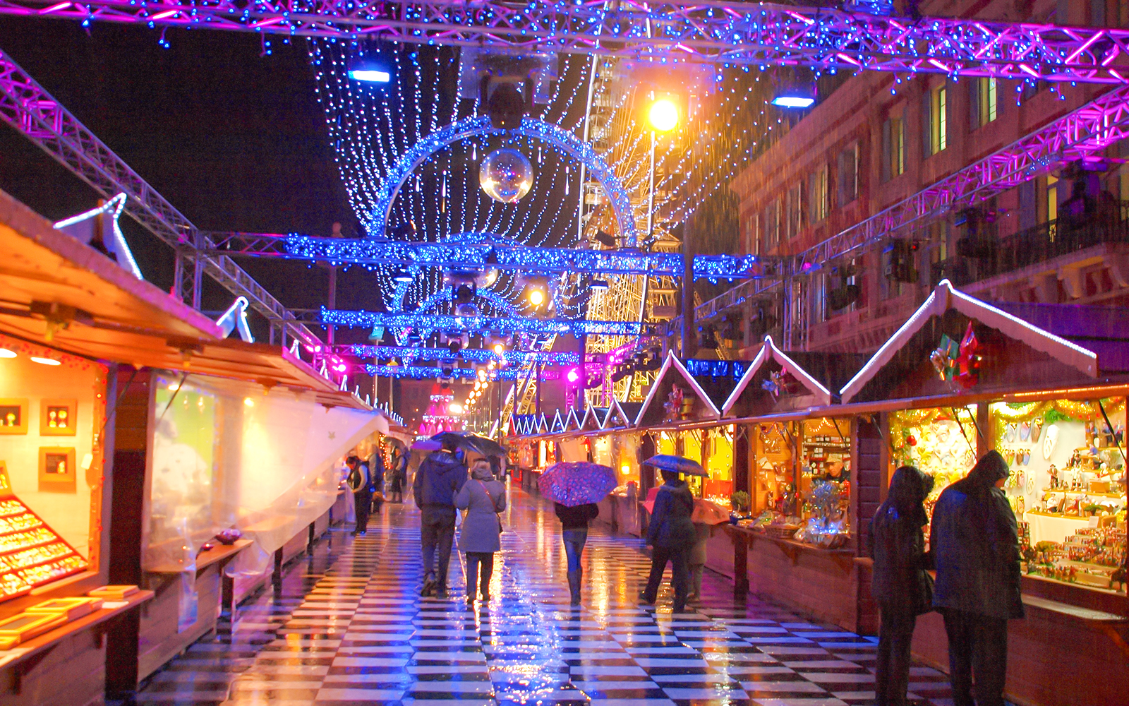 Christmas market in Nice with festive lights and people walking under umbrellas.