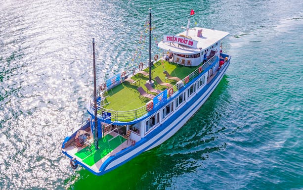 Deluxe cruise boat on Halong Bay with sun loungers and vibrant water.