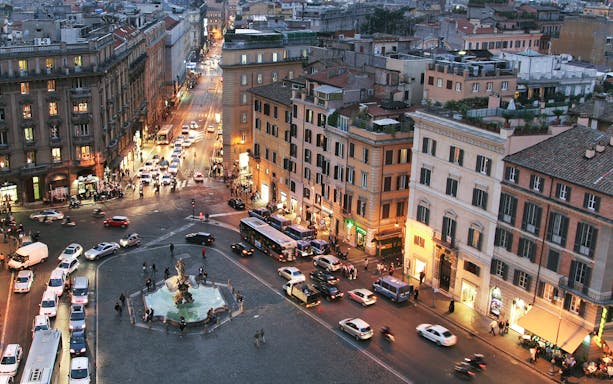 Barberini Square in Rome with Triton Fountain and surrounding buildings at dusk.