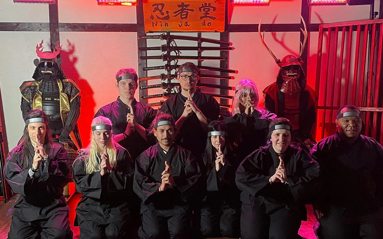 Participants in ninja attire at Osaka Ninja Workshop with samurai armor display.