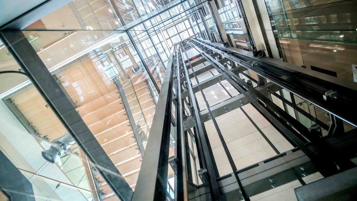 Glass elevator shaft interior with visible metal rails and reflections.