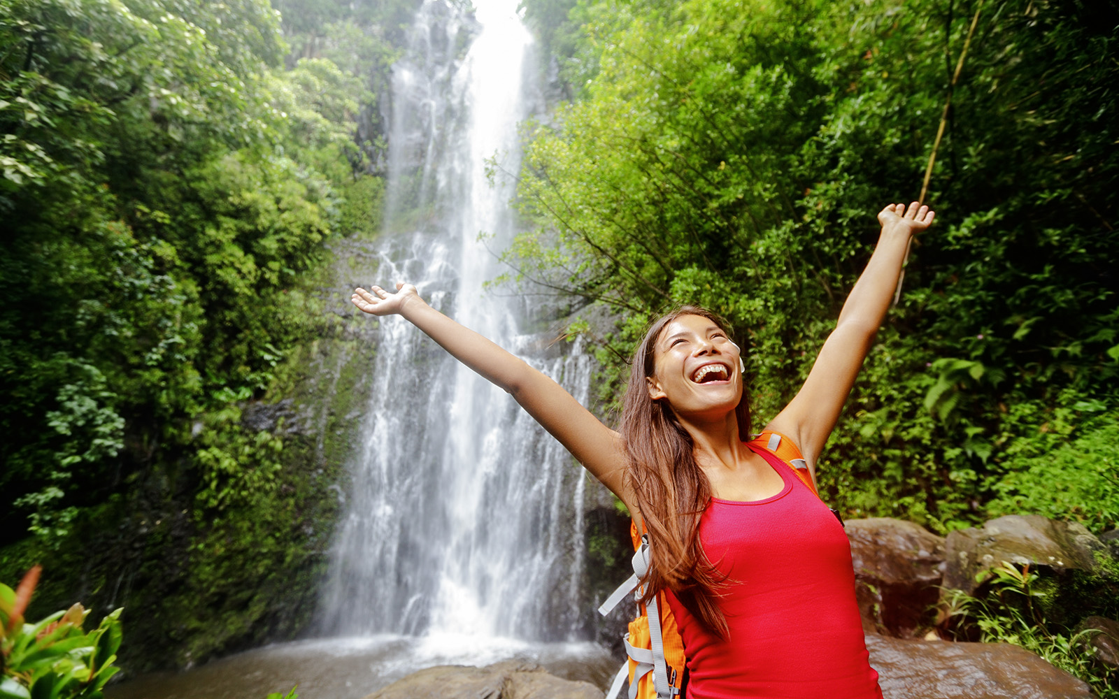 Woman smiling with arms raised in front of waterfall, Road to Hana, Hawaii.