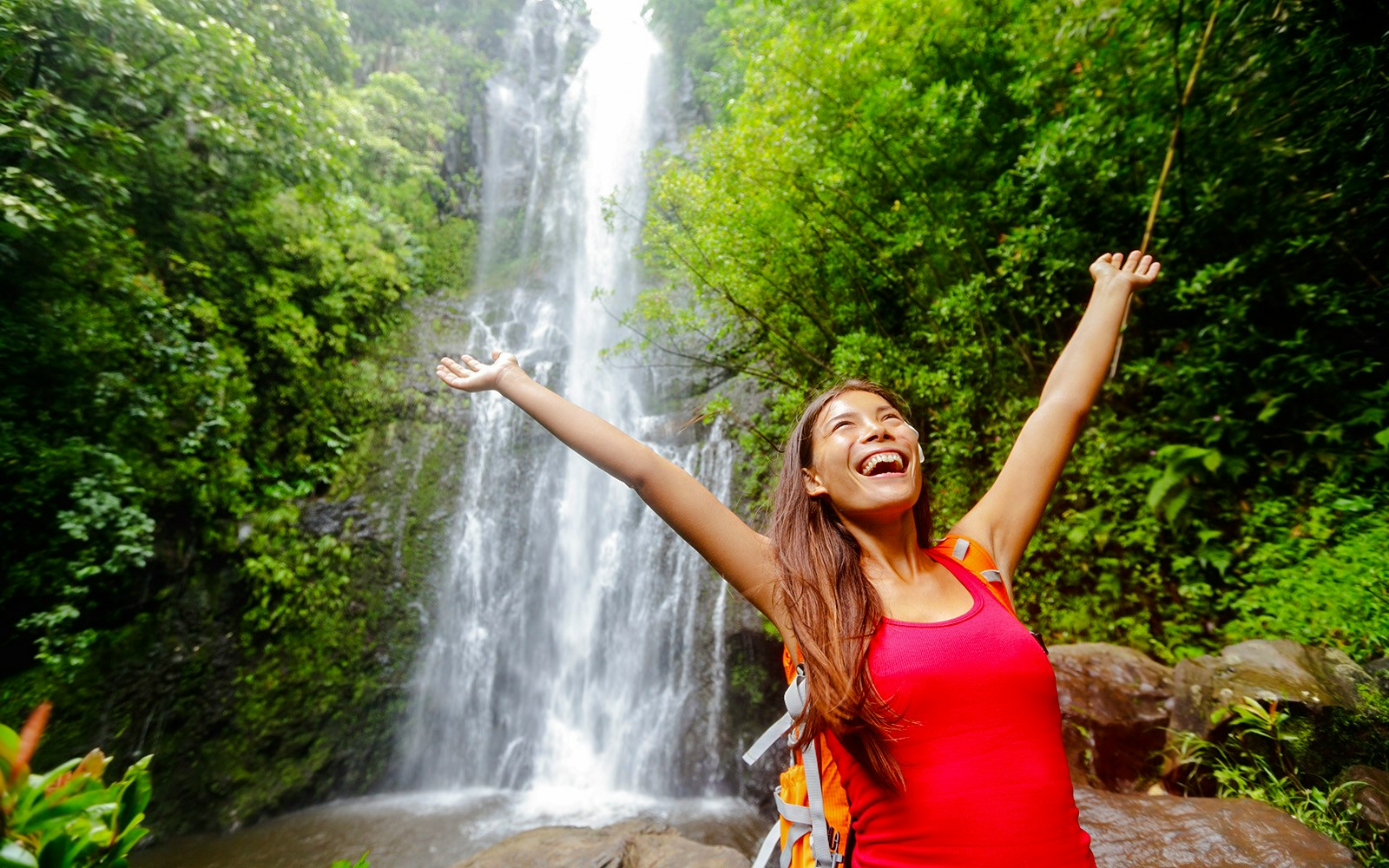 Woman smiling with arms raised in front of waterfall, Road to Hana, Hawaii.