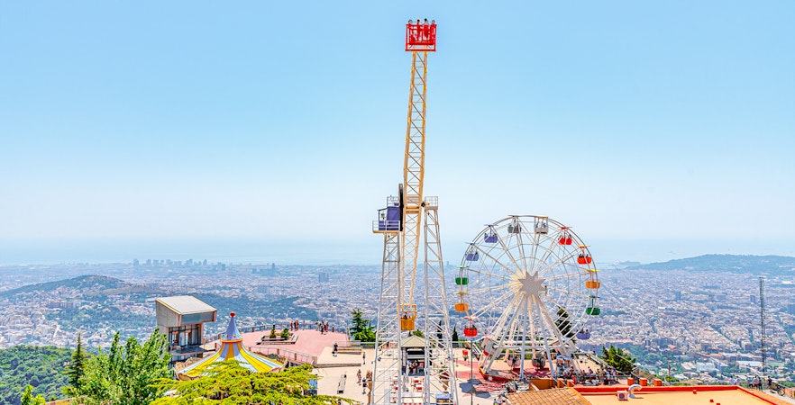 Tibidabo Amusement Park rides with panoramic view of Barcelona, Spain in the background.