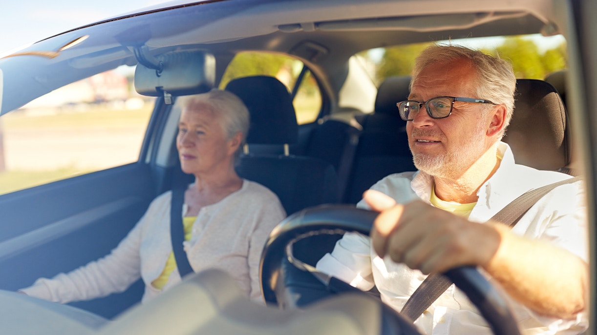 Senior couple driving in a car on a sunny day.