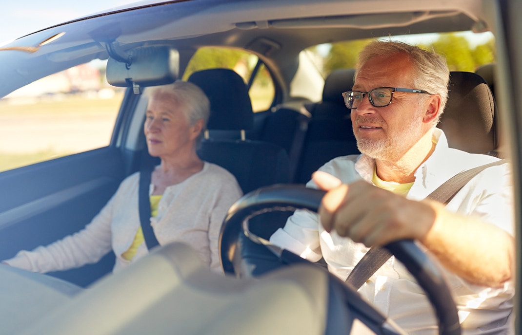 Senior couple driving in a car on a sunny day.