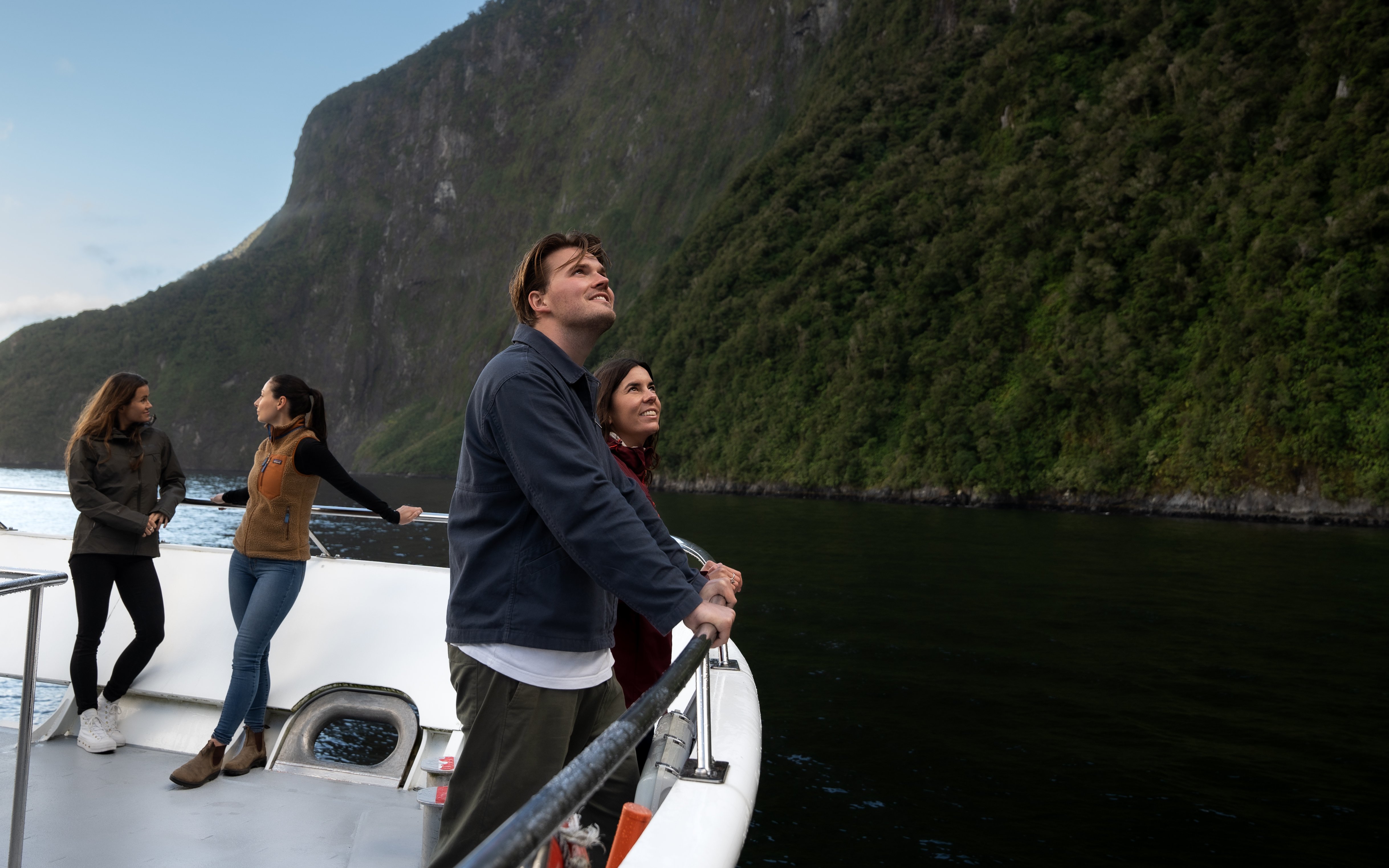Tourists on a boat enjoying views of Milford Sound cliffs in New Zealand.