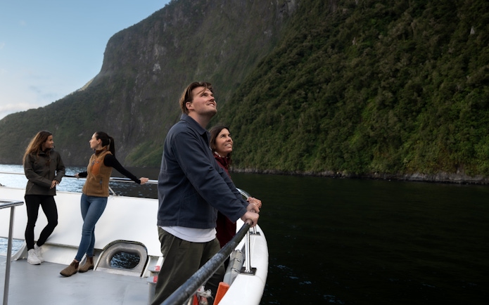 Tourists on a boat enjoying views of Milford Sound cliffs in New Zealand.