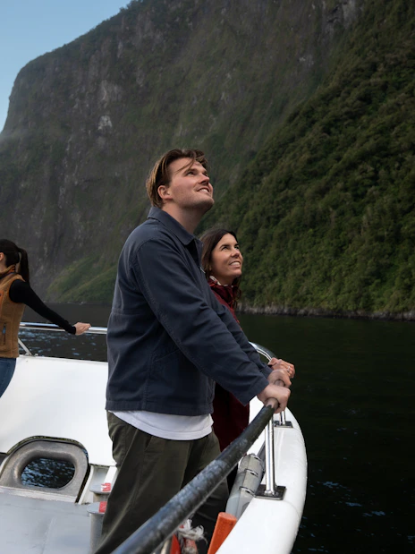 Tourists on a boat enjoying views of Milford Sound cliffs in New Zealand.