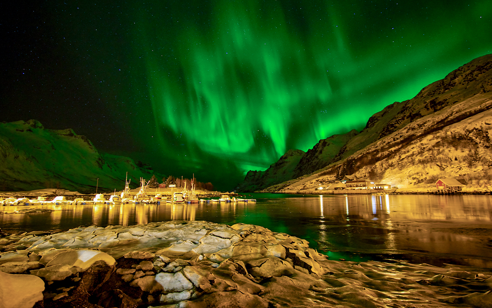 Ersfjordbotn northern lights illuminating sky above fishing boats in Norway.
