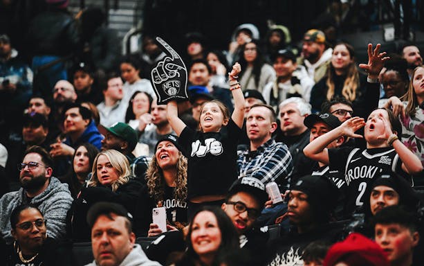Crowd cheering at a Brooklyn Nets game, child holding foam finger.