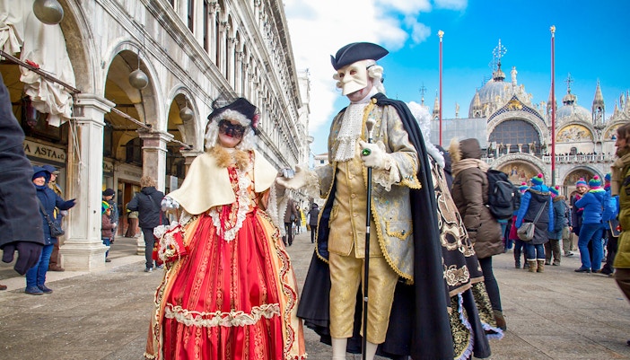 Venice Carnival participants in traditional masks and costumes in St. Mark's Square, Venice, Italy.