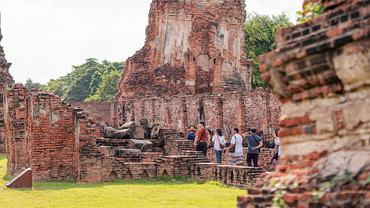 Tourists exploring Ayutthaya with guide near ancient temple ruins.
