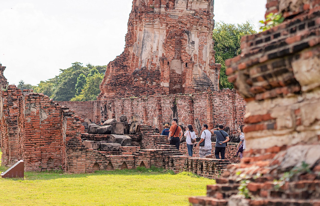 Tourists with guide exploring ancient ruins in Ayutthaya, Thailand.