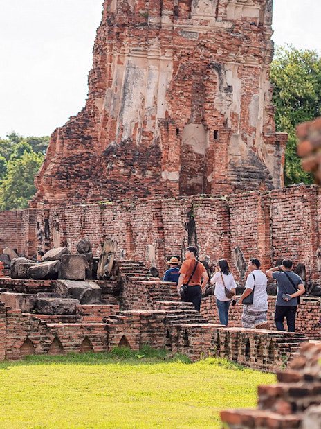 Tourists with guide exploring ancient ruins in Ayutthaya, Thailand.