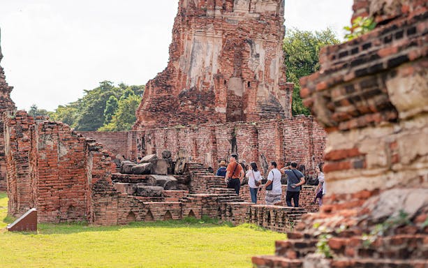 Tourists with guide exploring ancient ruins in Ayutthaya, Thailand.