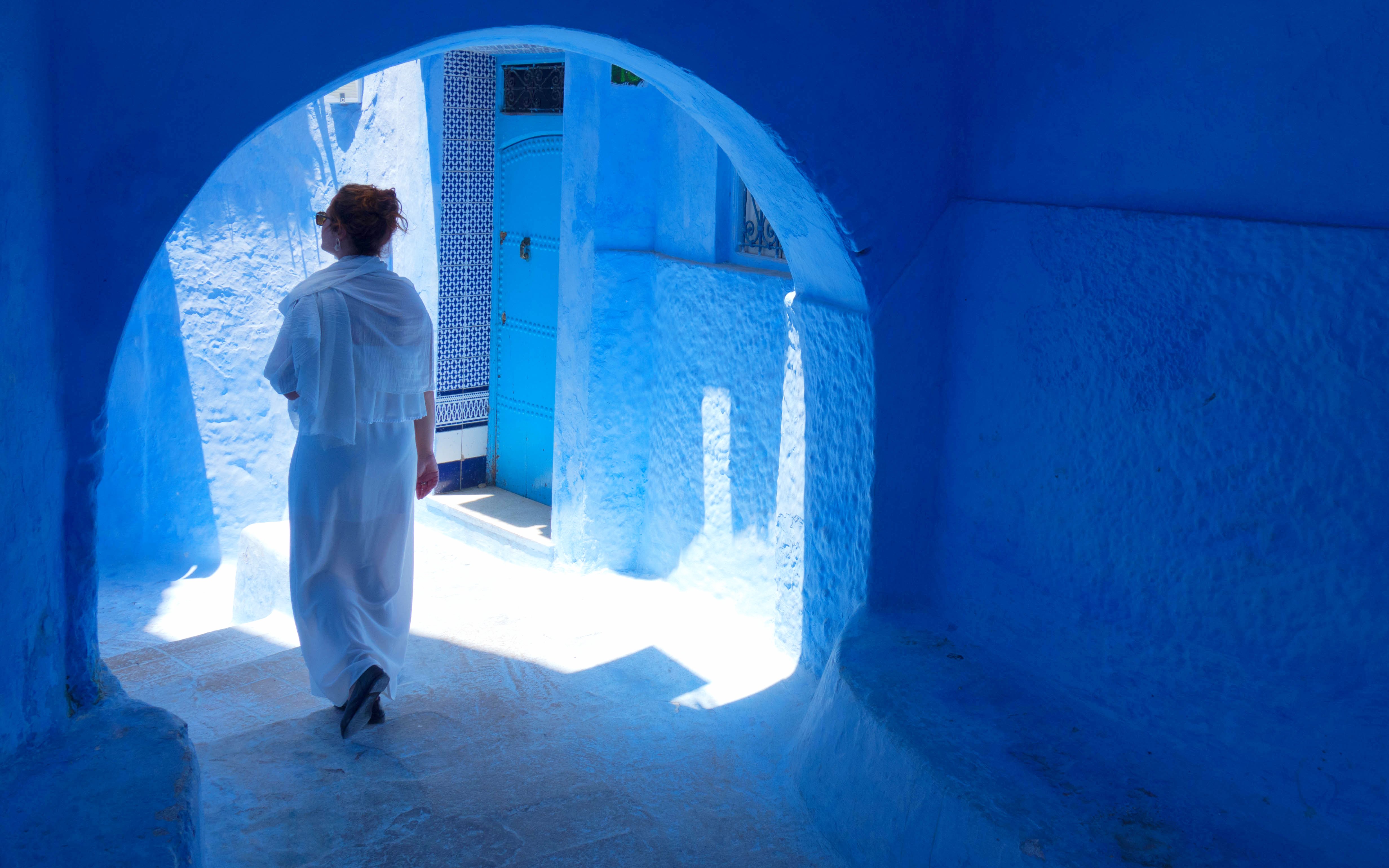 Woman walking through blue alley in Chefchaouen, Morocco.