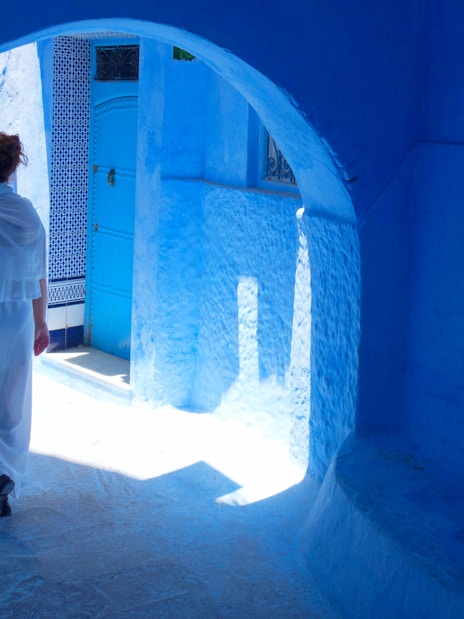 Woman walking through blue alley in Chefchaouen, Morocco.