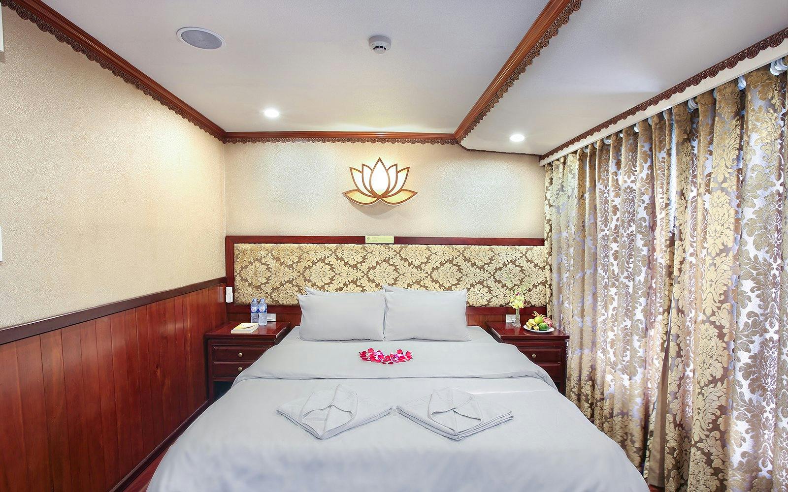 Cruise cabin with double bed, floral decor, and fruit platter on Halong Bay 3-star cruise.