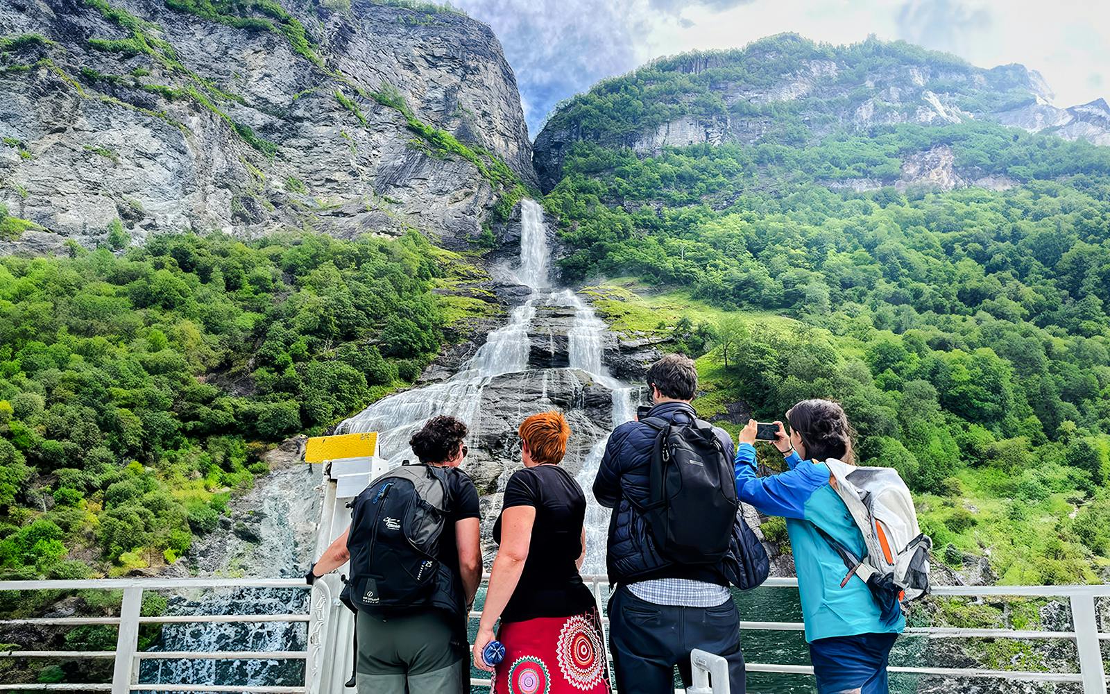 Tourists on a boat admire a waterfall in Geiranger Fjord, Norway.