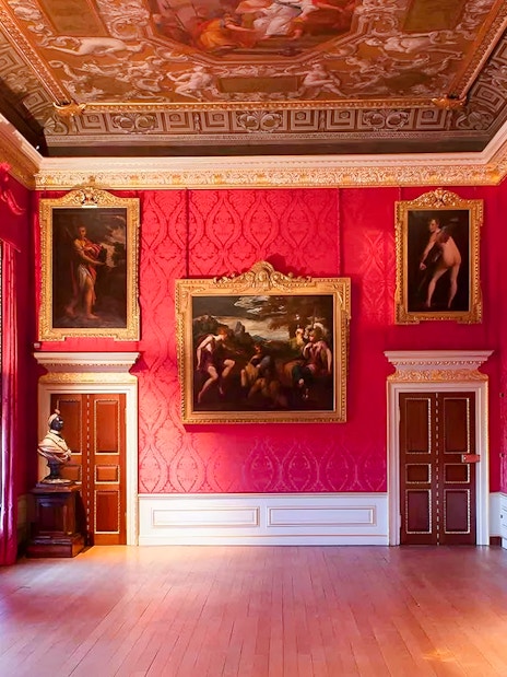 Kensington Palace interior with ornate paintings and red walls.