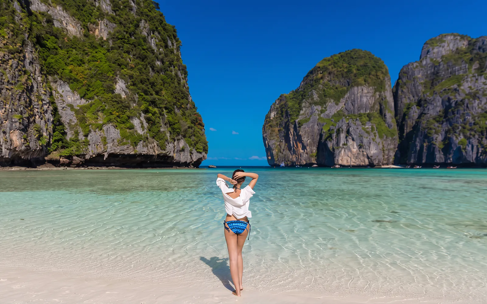 Person standing on Maya Bay beach with limestone cliffs, Phi Phi Islands, Thailand.