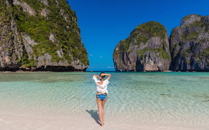 Person standing on Maya Bay beach with limestone cliffs, Phi Phi Islands, Thailand.