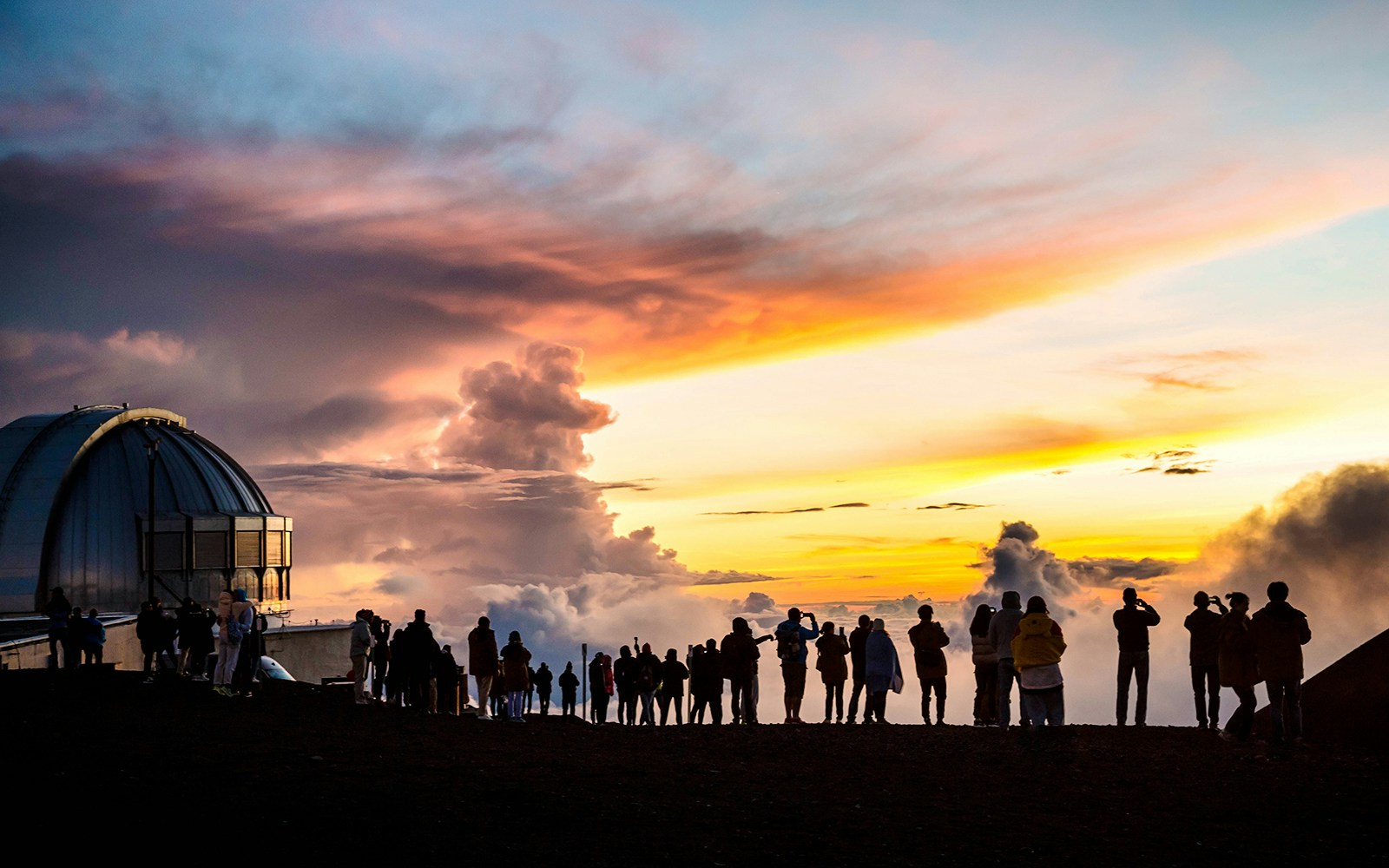 Visitors at Mauna Kea Summit observing sunset near observatory dome, Hawaii.