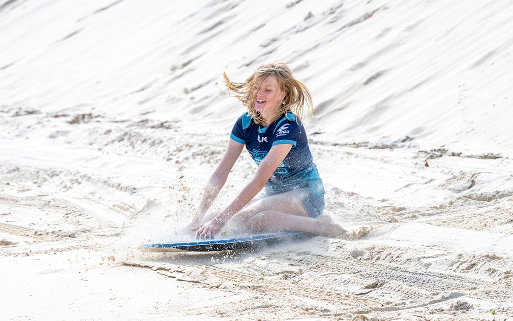 Person sandboarding on Moreton Island during a 4WD desert adventure.