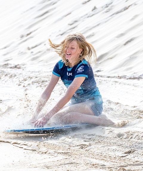 Person sandboarding on Moreton Island during a 4WD desert adventure.