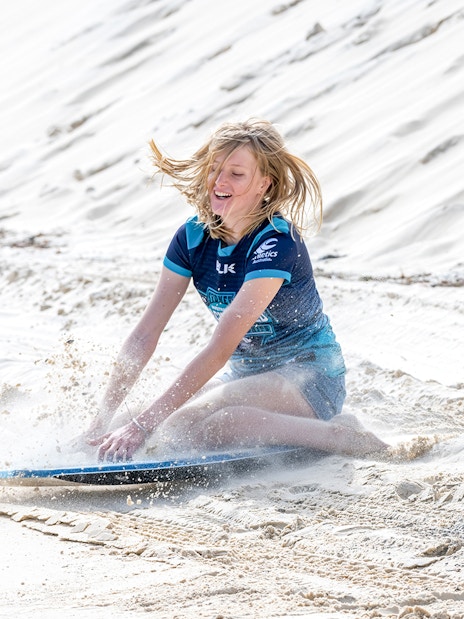 Person sandboarding on Moreton Island during a 4WD desert adventure.