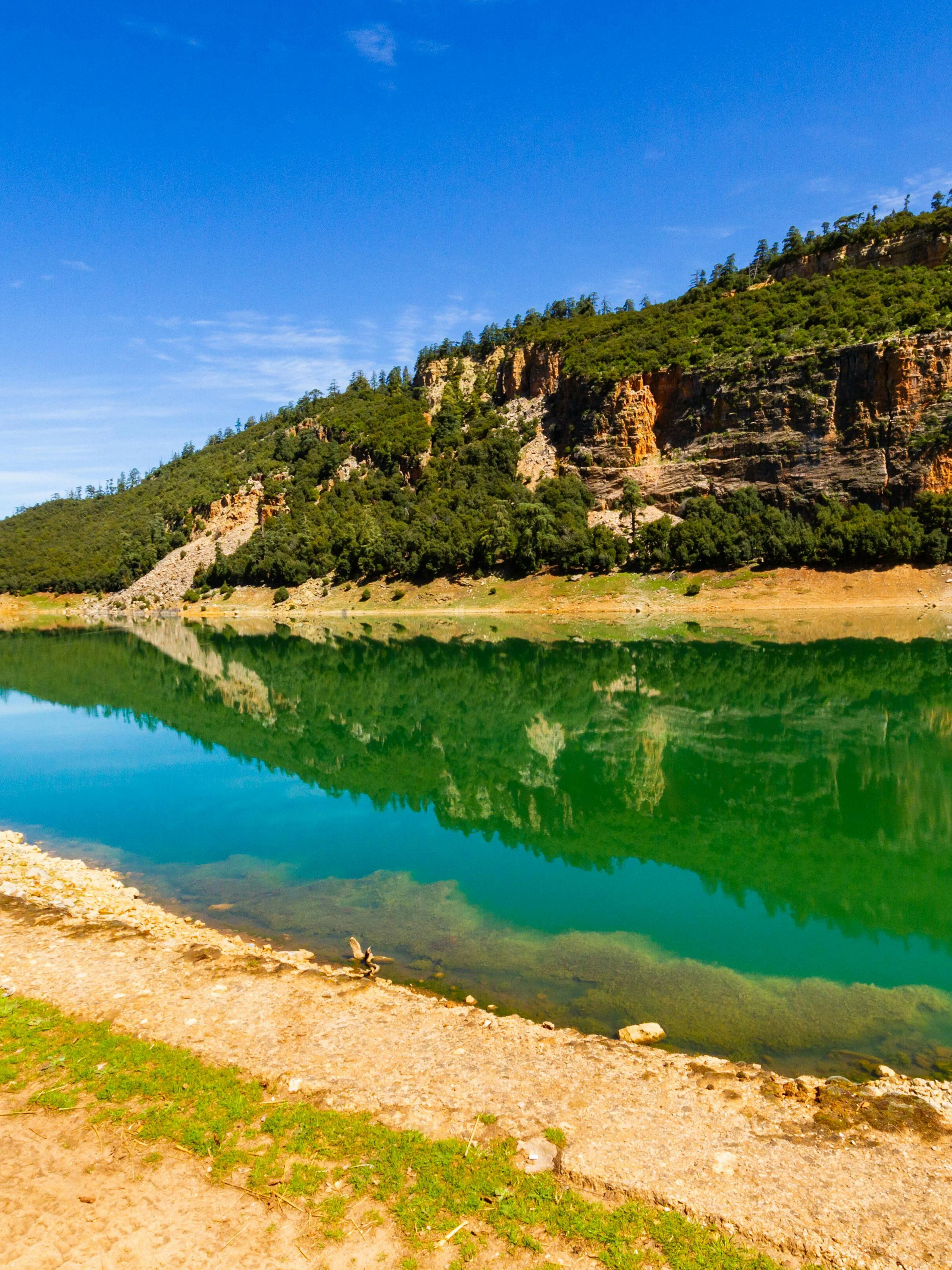Reflection of Middle Atlas Mountains on a tranquil lake under a clear blue sky.