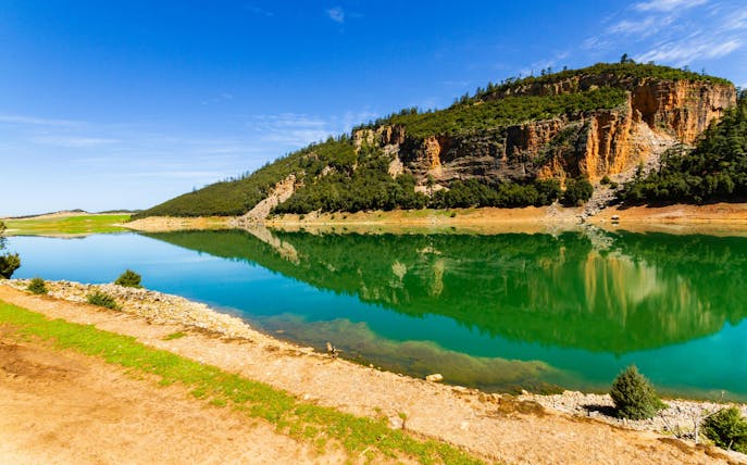 Reflection of Middle Atlas Mountains on a tranquil lake under a clear blue sky.