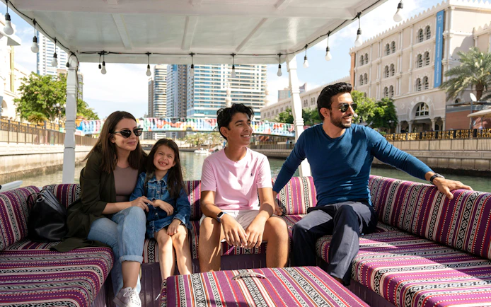 Family enjoying a boat tour on a canal in Sharjah with cityscape views.