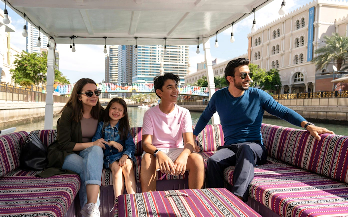 Family enjoying a boat tour on a canal in Sharjah with cityscape views.