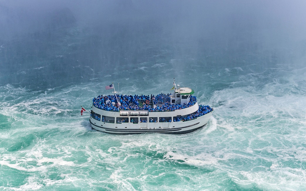 Tour boat near Niagara Falls with passengers in blue ponchos, USA.