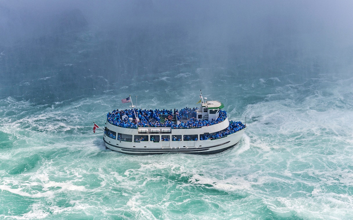 Tour boat near Niagara Falls with passengers in blue ponchos, USA.
