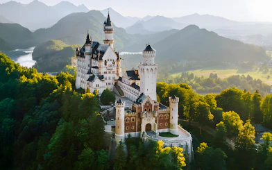 Aerial view of Neuschwanstein Castle surrounded by lush green forests and mountains.
