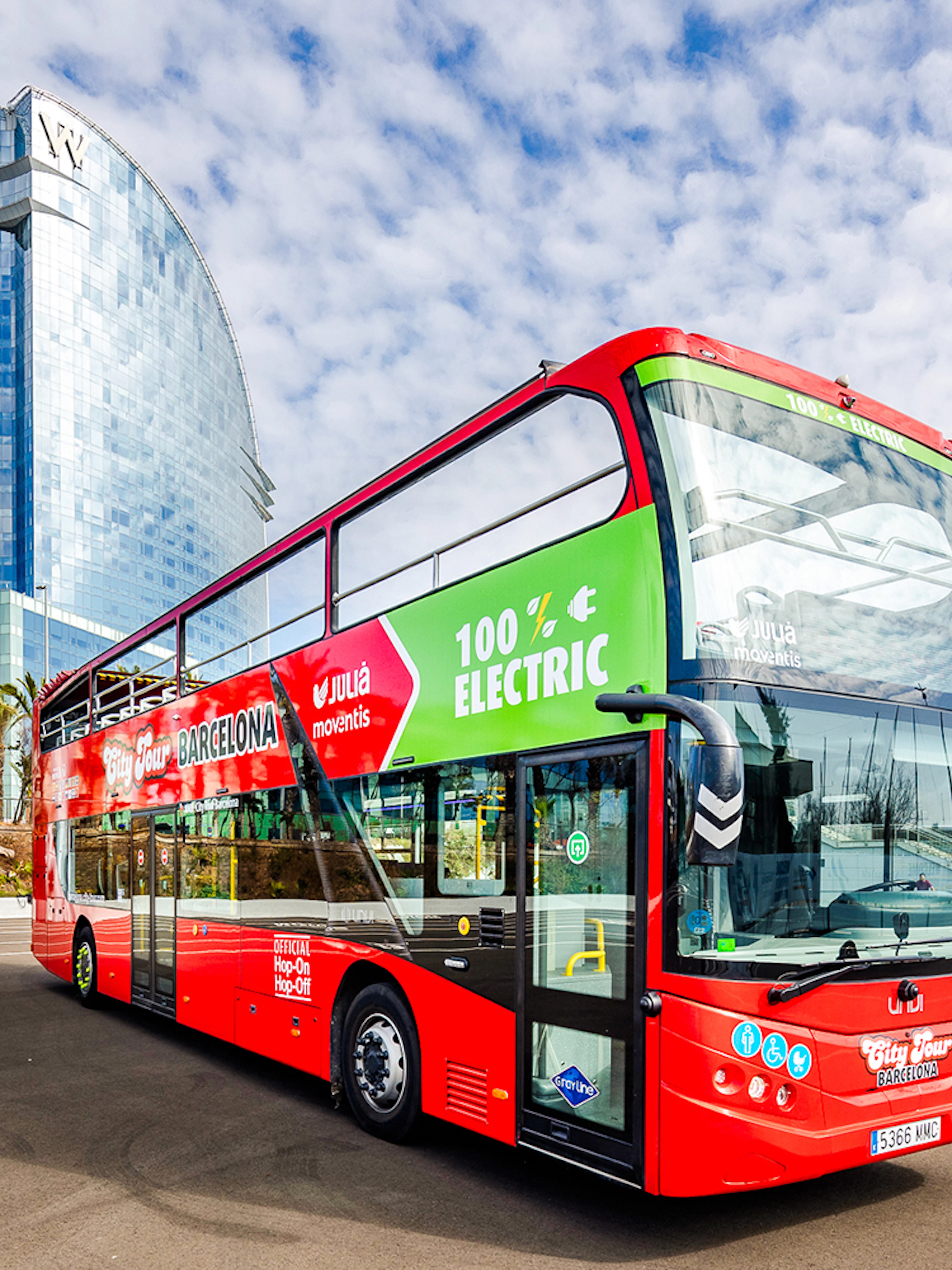 Red double-decker bus for Barcelona hop-on hop-off tour near modern glass building.