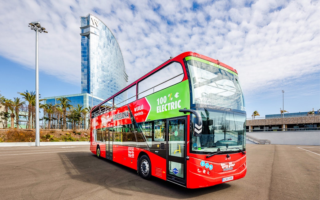 Red double-decker bus for Barcelona hop-on hop-off tour near modern glass building.
