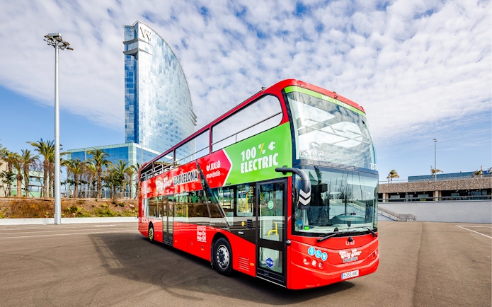 Red double-decker bus for Barcelona hop-on hop-off tour near modern glass building.