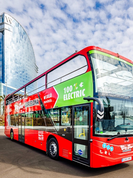 Red double-decker bus for Barcelona hop-on hop-off tour near modern glass building.