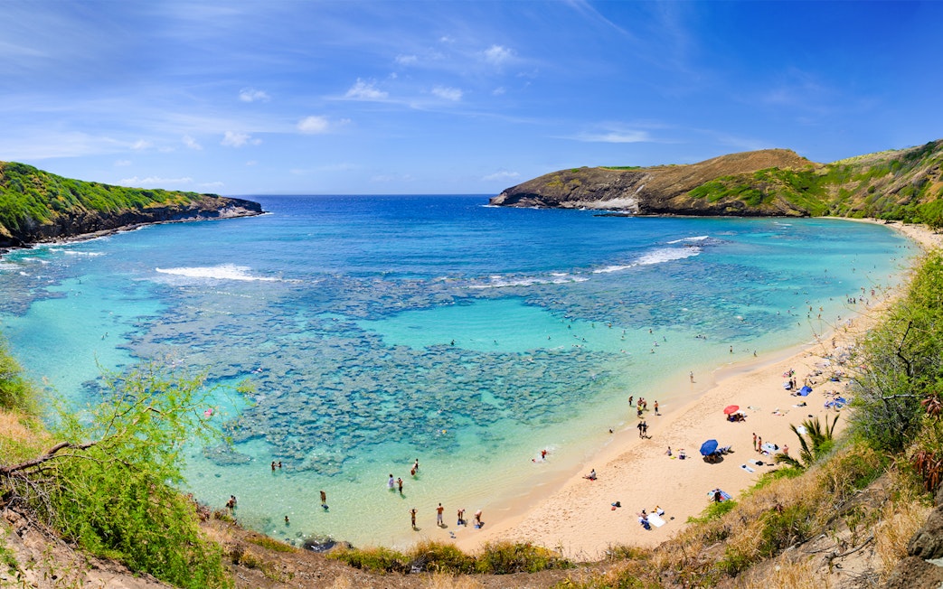 Aerial view of Hanauma Bay, Hawaii, with people on the sandy shore and clear blue water.