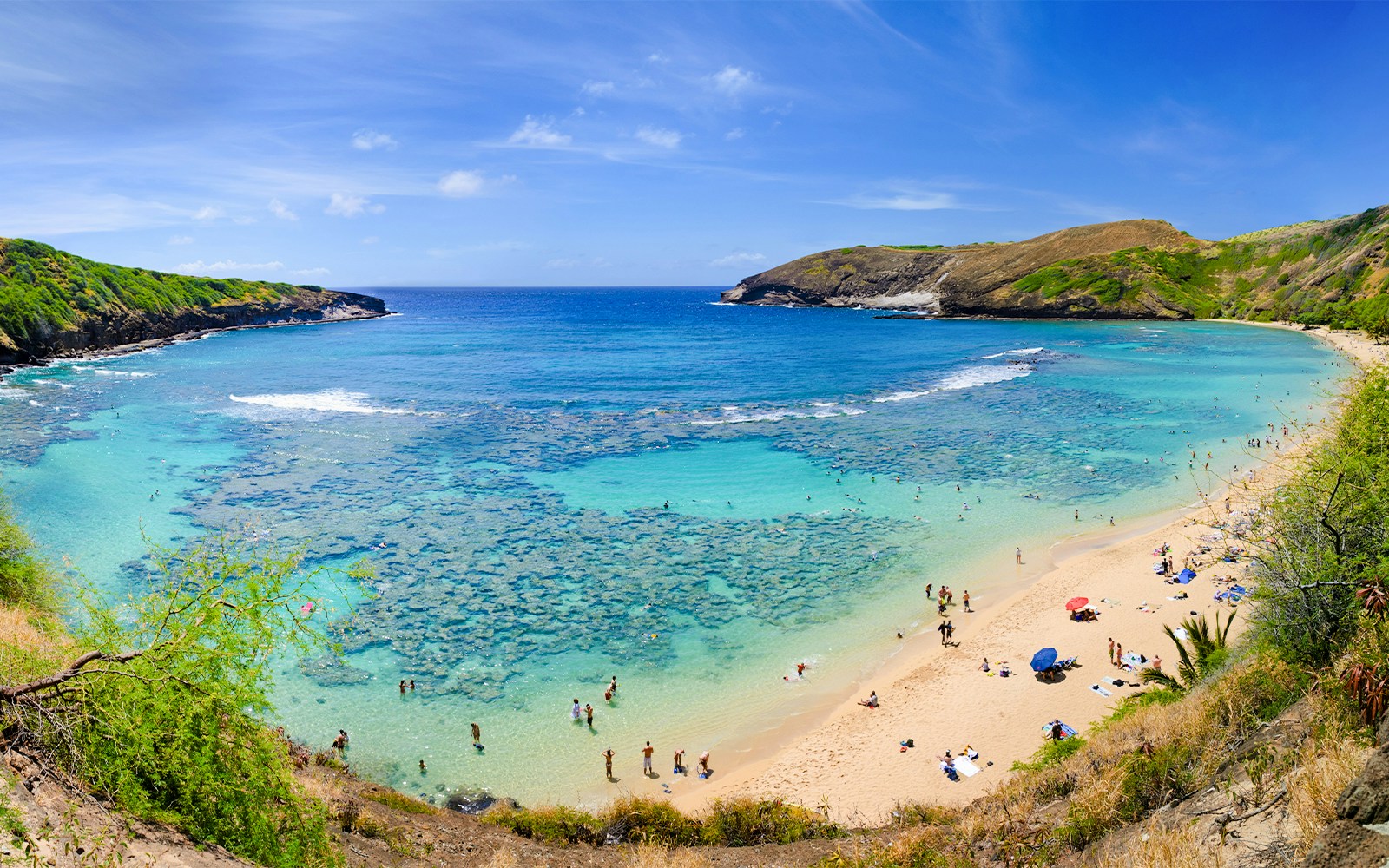 Aerial view of Hanauma Bay, Hawaii, with people on the sandy shore and clear blue water.