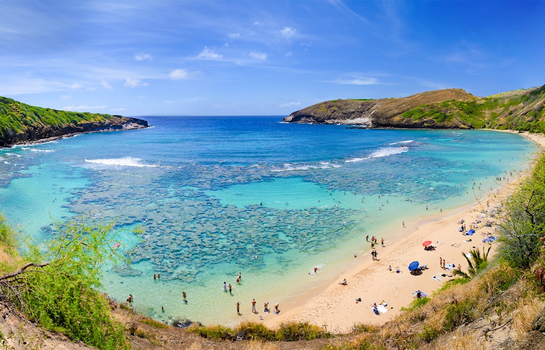 Aerial view of Hanauma Bay, Hawaii, with people on the sandy shore and clear blue water.