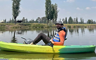Kayaker on Xochimilco canal with local guide, surrounded by trees and calm water.