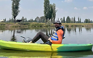 Kayaker on Xochimilco canal with local guide, surrounded by trees and calm water.