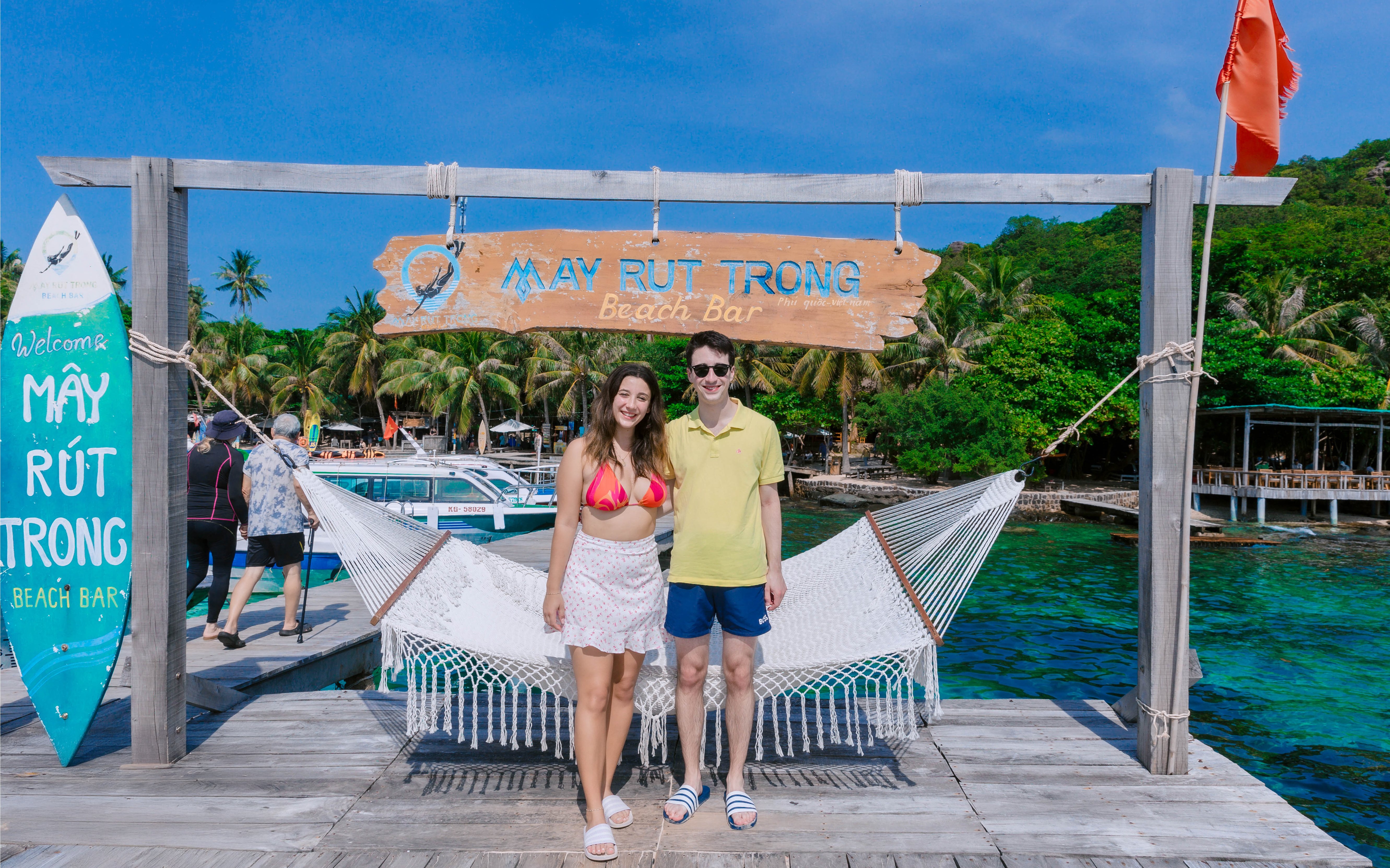 Couple standing on a dock in front of May Rut Trong Island Beach Bar, Vietnam.