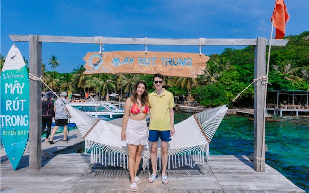Couple standing on a dock in front of May Rut Trong Island Beach Bar, Vietnam.