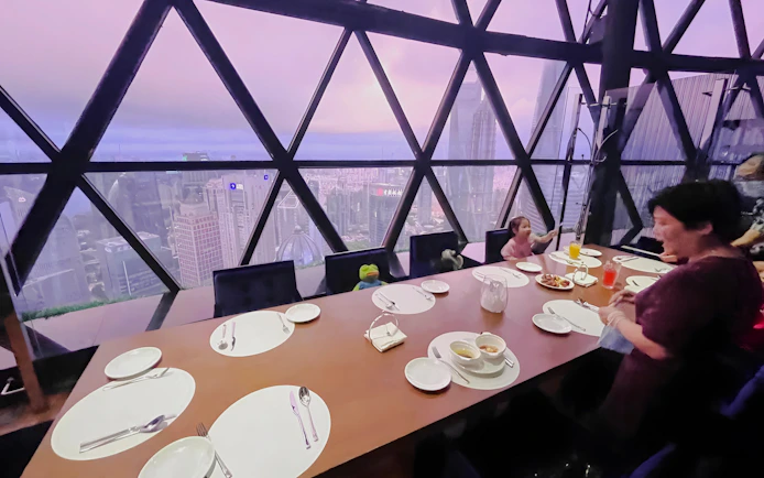 Family dining at revolving restaurant, Oriental Pearl Tower, Shanghai, with city skyline view.